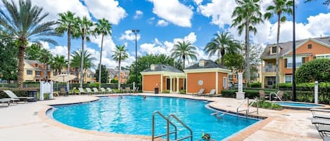 Piscina com espreguiçadeiras e palmeiras, rodeada por edifícios.