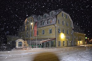 A multi-story building with a snow-covered roof, a visible entrance, and a sign indicating a restaurant or dining area.