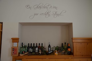 A wine display with bottles and glasses on a wooden shelf against a wall with a decorative sign. - Standard Double Room - Kirchenwirt Aigen (Aigen im Ennstal)