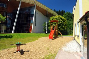 Un terrain de jeux avec un toboggan et des balançoires, un bâtiment doté de grandes fenêtres et un ciel dégagé.