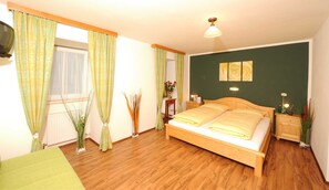 Un dormitorio con cama de madera, cortinas verdes, una mesita de noche con lámpara, un mueble auxiliar y una lámpara de pared.