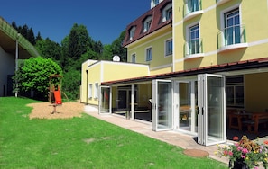 A yellow building with a red roof, a covered patio area, and a playground. - Standard Single Room - Kirchenwirt Aigen (Aigen im Ennstal)