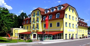 En gul byggnad med ett rött markis, en flagga och en skylt med texten ”Kirchenwirt”.