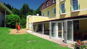 A yellow building with a red roof, a covered patio area, and a playground. - Standard Single Room - Kirchenwirt Aigen (Aigen im Ennstal)