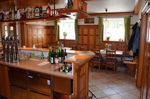 A kitchen with a bar area, wooden cabinets, a dishwasher, and a dining table with chairs. - Comfort double room - Kirchenwirt Aigen (Aigen im Ennstal)