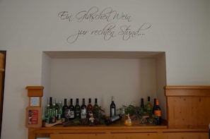Wijnrek met flessen en glazen op een houten plank tegen een muur met een decoratief bord.