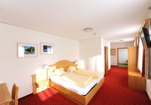 Una habitación de hotel con cama, escritorio, silla, televisor y dos cuadros en la pared.
