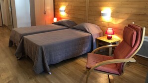 Una habitación con dos camas, un armario de madera, una mesita con una lámpara y una silla.