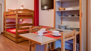 A bunk bed with a TV above it, a table with cups and a red placemat, and shelves with plates and bowls. - Renovated studio for 4 people with washer, wifi (Brides-les-Bains)