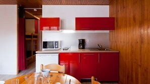 Une cuisine compacte avec des meubles rouges, un four à micro-ondes, une machine à café et une table à manger avec des chaises.