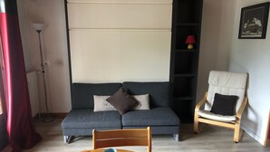 Un salon chaleureux avec un canapé, un fauteuil, une table sur laquelle se trouvent une théière et des tasses, et une lampe sur pied.