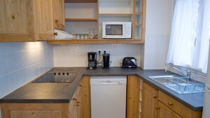 Een kleine keuken met houten kastjes, een magnetron, een koffiezetapparaat, een broodrooster en een vaatwasser.