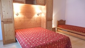 Een slaapkamer met een groot bed, een kleiner bed, houten kasten en een wandplank.