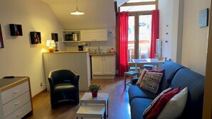Un espacio habitable compacto con kitchenette, comedor y zona de estar con sofá y sillón.