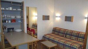 Una habitación compacta con kitchenette, un sofá, una mesita y una silla.