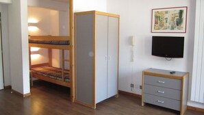 Una habitación con una cama litera, un armario, un escritorio y un televisor instalado en la pared.