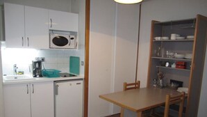 Cocina compacta con armarios blancos, microondas, cafetera y refrigerador pequeño.