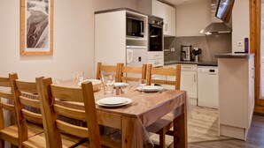 A dining area with a wooden table set for two, a kitchen with modern appliances, and a framed picture on the wall. - 4-room apartment with balcony, internet, parking in the center of Brides-les-Bains (Brides-les-Bains)