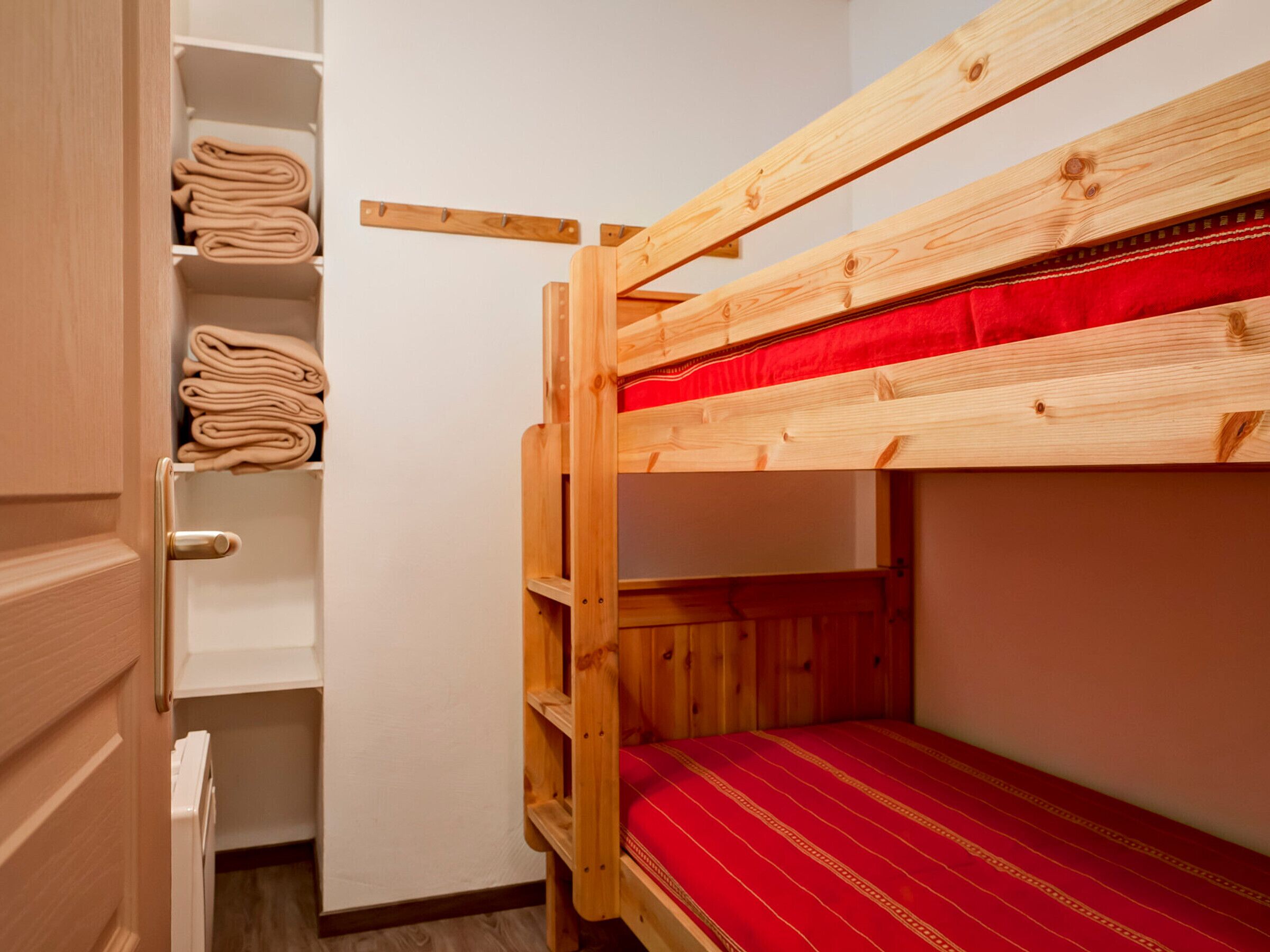 A bunk bed with a red mattress, wooden headboard, and a shelf unit with folded towels.