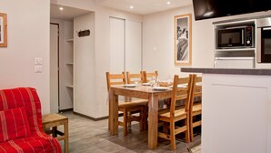 A dining area with a wooden table and chairs, a red armchair, a television mounted above the counter, and a microwave. - 4-room apartment with balcony, internet, parking in the center of Brides-les-Bains (Brides-les-Bains)