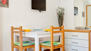 A small, clean room with a white table, two wooden chairs, a TV mounted on the wall, and a mirror above the table. - 2* Studio with Wifi in Brides-les-Bains Center (Brides-les-Bains)