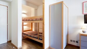 A room with a bunk bed, a desk with a lamp, and a TV on the wall. - Studio for 4 with Balcony, WiFi & Parking (Brides-les-Bains)