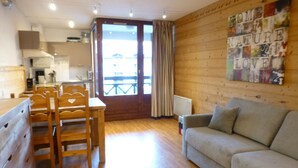 A cozy living room with a sofa, wooden dining table, and chairs. A kitchen is visible in the background. - Studio for 4 with Wifi and Parking - Brides-les-Bains (Brides-les-Bains)
