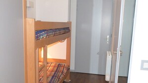 A bunk bed with plaid bedding in a room with a wooden floor and a closed door. - Studio for 4 - City Center, Balcony, Wi-Fi (Brides-les-Bains)