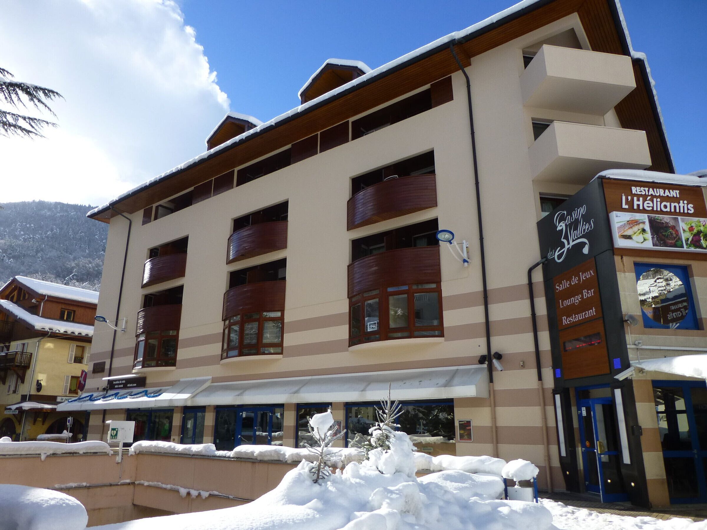 Un immeuble à plusieurs étages doté de balcons, une enseigne indiquant un restaurant et un paysage enneigé.