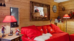 Una habitación acogedora con detalles de madera, un sofá rojo con una manta de piel blanca, un escritorio de madera con una lámpara y un espejo en la pared.