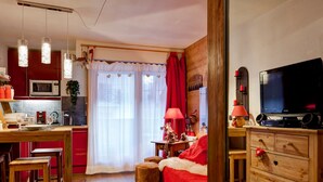 Una habitación acogedora con un escritorio de madera, televisor, un sofá rojo y una zona de cocina con microondas.