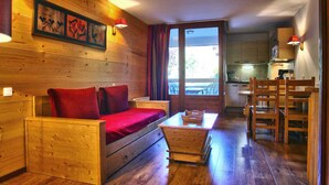 A wooden cabin interior with a sofa bed, a small table, and a kitchen area. - Cozy Studio with WiFi and Parking - Sleeps 4 (Brides-les-Bains)