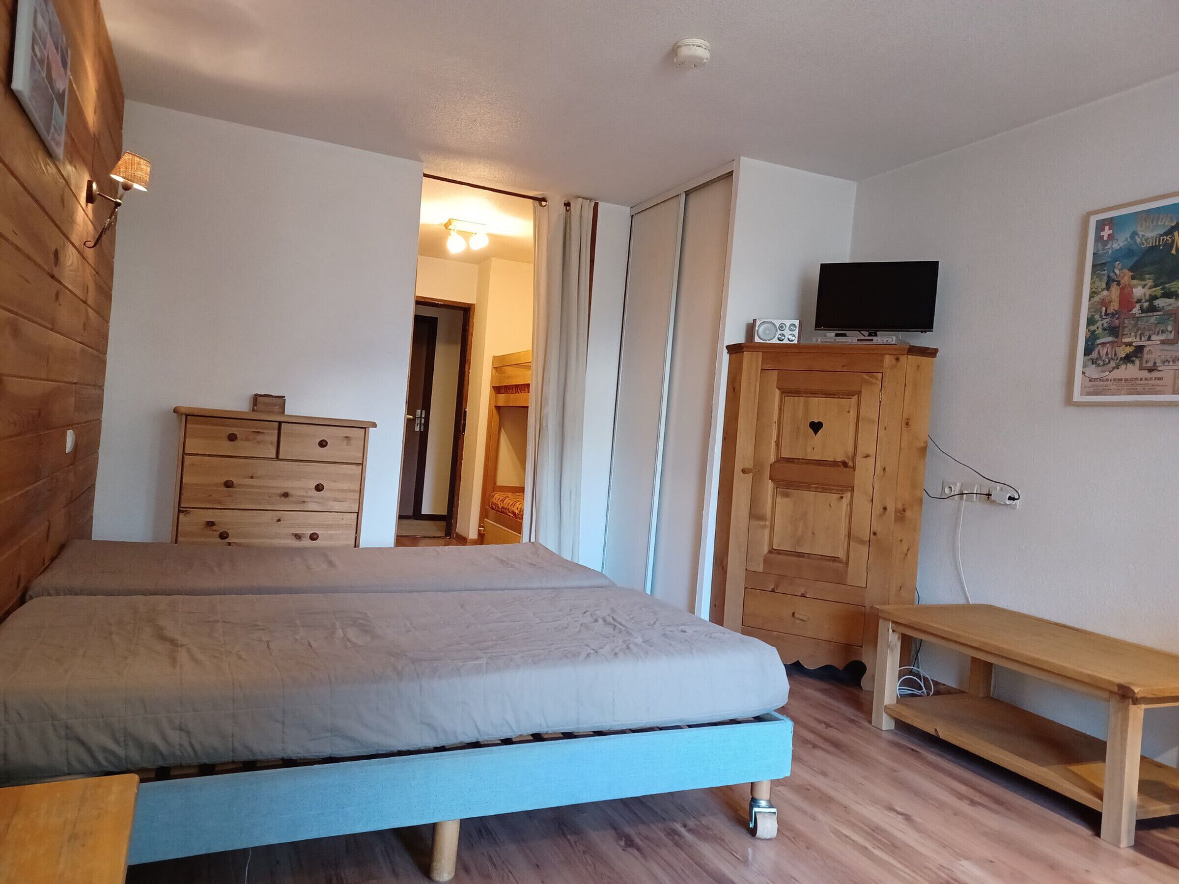 A bedroom with a bed, wooden dresser, TV, and a painting on the wall.