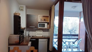 A compact kitchen with a microwave, sink, and a small refrigerator. There is a wooden table and chairs, and a balcony with a view of trees. - 2* Studio for 4 with mountain view, parking included, pets allowed (Brides-les-Bains)