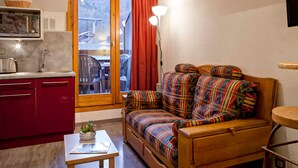 A compact living space with a kitchenette, a sofa with colorful upholstery, a small table with a plant, and a window with curtains.