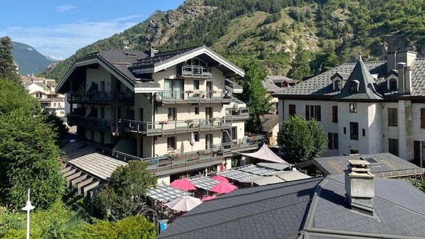 Un immeuble à plusieurs étages doté de balcons, entouré d’une végétation luxuriante et avec des montagnes en arrière-plan.