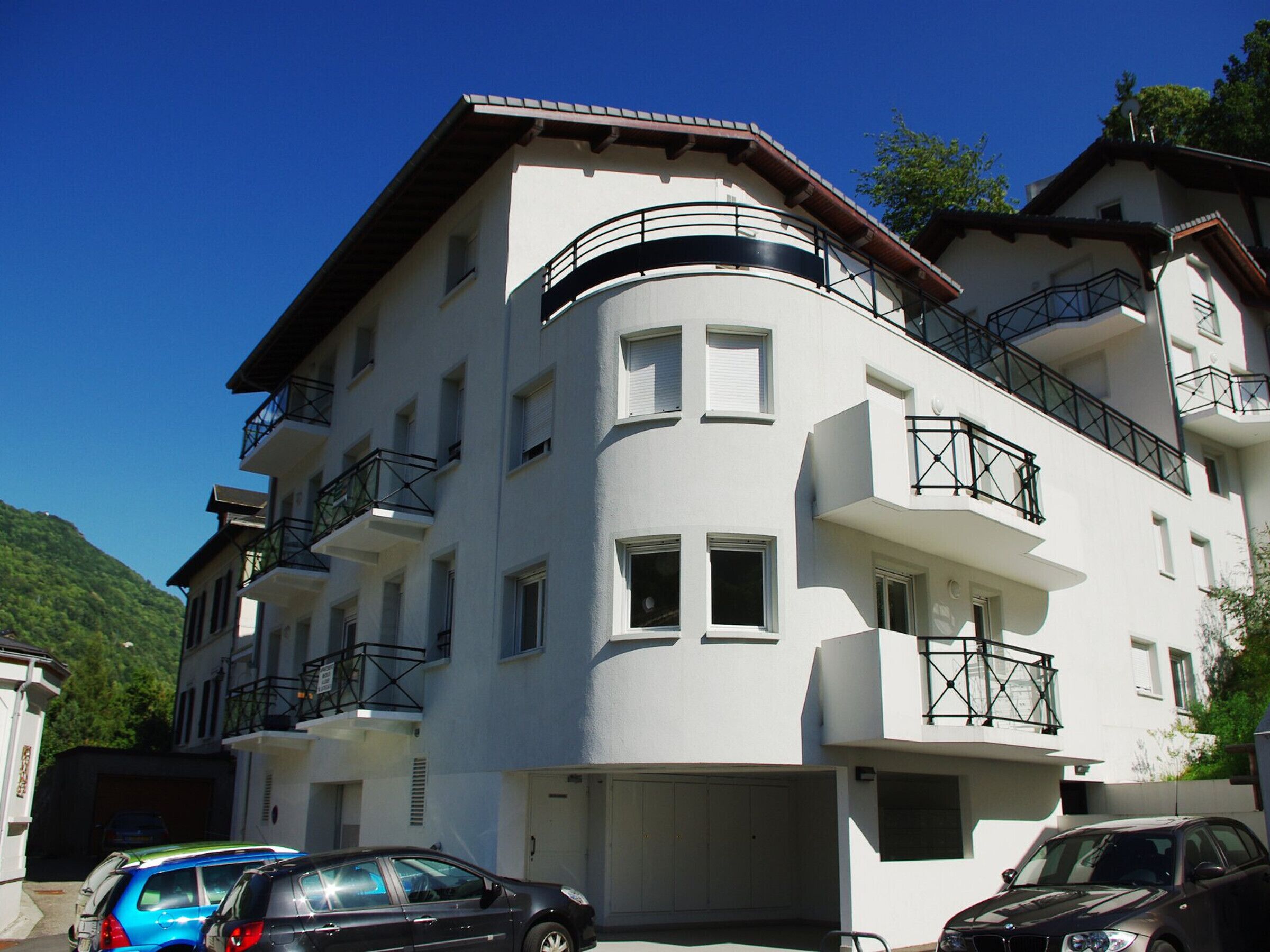 Ein mehrgeschossiges Gebäude mit Balkonen, einer Garage und einem geparkten Auto davor.