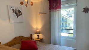 Une chambre à coucher avec une tête de lit en bois, un oreiller rouge, une lampe de chevet et une fenêtre donnant sur un immeuble.