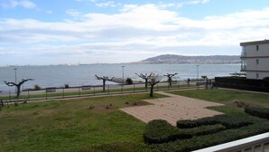 A coastal view with a paved walkway, trees, and a building in the background. - Apartment with Balcony 5 min from Spa - Pets allowed (Balaruc-les-Bains)