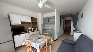 A compact kitchen with a dining table, chairs, a sofa, and a ceiling fan. - Apartment with Balcony 5 min from Spa - Pets allowed (Balaruc-les-Bains)