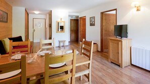 Un comedor con una mesa y sillas de madera, un televisor sobre un mueble de madera, y un radiador blanco en la pared.