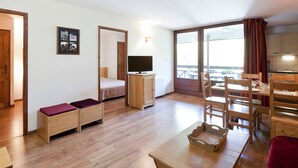Un espacio habitable pequeño con cama, televisor, mesa de comedor con sillas y balcón con vistas.
