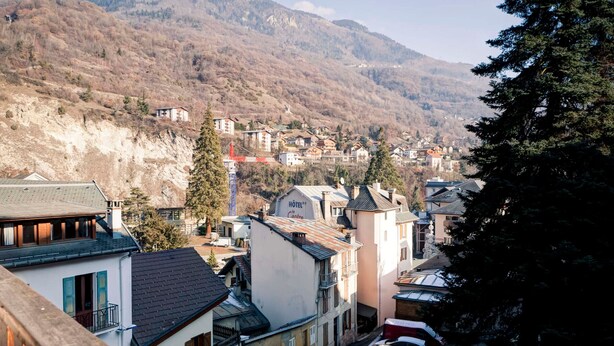 Un hotel con un cartel visible, una calle con coches aparcados y un telón de montañas al fondo.