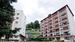 Un hotel de varios pisos con balcones, un estacionamiento y un paisaje montañoso de fondo.