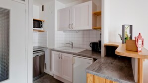 Cocina compacta con armarios blancos, microondas, pileta y cafetera.
