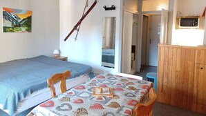 Un dormitorio con una cama, una mesa con mantel estampado, un armario de madera, un esquí en la pared y un cuadro.