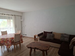 Uma sala de estar com sofá, mesa de centro, mesa de jantar e cadeiras, e uma janela com cortinas.