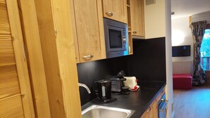 Una cocina compacta con armarios de madera, un microondas, un hervidor, un tostador y un lavamanos.