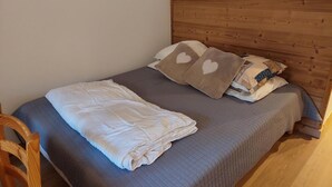 Una cama individual con cabecera de madera, edredón acolchado gris y dos almohadas con diseño de corazones.