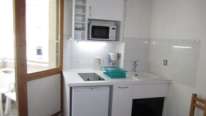 Cocina compacta con microondas, lavamanos y refrigerador pequeño.